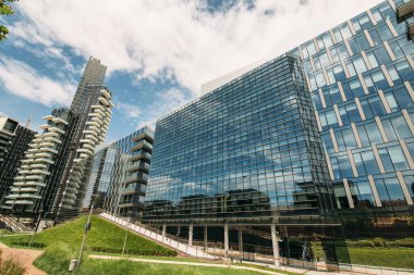 Ön planda büyük cam bina. Arka planda yeşil çimen. Mavi gökyüzü ve Clou.