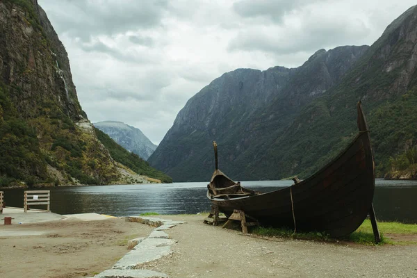 Nehrin arka planında eski Norveç Viking teknesi, dağlar ve mavi gökyüzü.