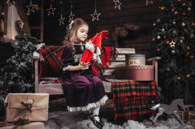 Noel kostümlü bir kız, fındık kıracağını bir bankın arka planında, Noel ağacında ve solmuş yıldızlı bir duvarda tutar.