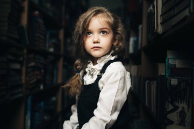 Okul üniformalı bir kız kitaplarla, okulla, librar arasında bir taburede oturuyor.