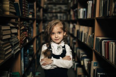 Okul üniformalı bir kız kitaplarla, okulla, librar arasında duruyor.