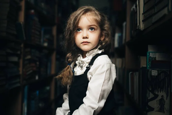 Okul üniformalı bir kız kitaplarla, okulla, librar arasında bir taburede oturuyor.