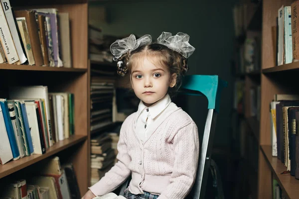 first grader sits on a chair in the library and holds a book in her hands