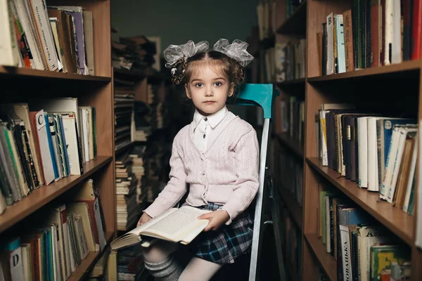 first grader sits on a chair in the library and holds a book in her hand