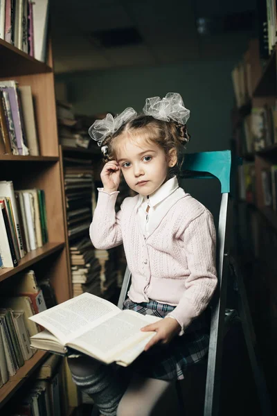 first grader sits on a chair in the library and holds a book in her hand