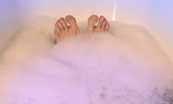 Feet in the bathtub stock images. Bath with foam images. Colored bath foam with feet. Female feet taking a bath