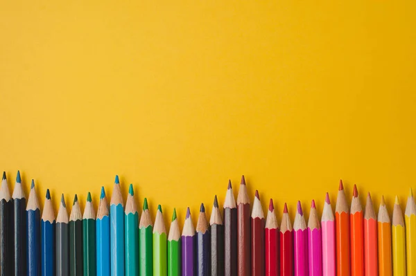 Hardal bir arka plan üzerinde renkli kalemler.