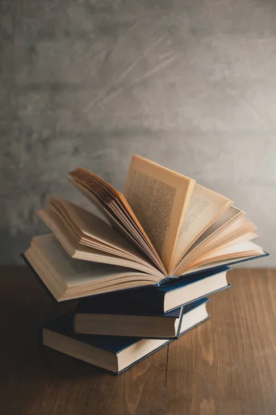 Stack of books on a wooden table and on gray concrete wall backg — Stock Photo, Image