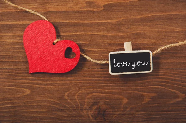 kırmızı kalp bir ipte ve küçük kara tahta üzerinde ahşap bir arka planda seni seviyor. Sevgililer Günü kompozisyonu.