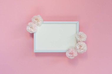 Flat lay - white blank frame with pink carnations on a pink back