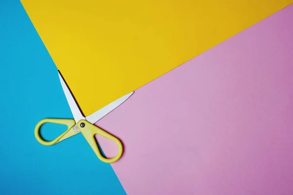 Sarı makas pembe, mavi ve sarı arka planda kesilmiş. Yaratıcı geometrik kavram. Düz yat, boşluğu kopyala.