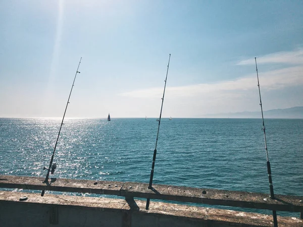 Rybářské pruty se čeká na kousání na molu. Na pozadí plachetní jachty. Teplý letní den v Kalifornii, Usa — Stock fotografie