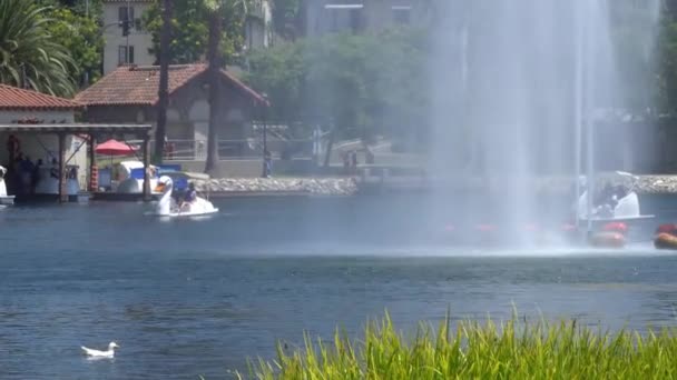 LOS ÁNGELES, CALIFORNIA, EE.UU. - 28 de agosto de 2019: Echo Park Lake. Los chorros de la fuente golpearon alto. La gente va en bote. Cálido día soleado . — Vídeo de stock