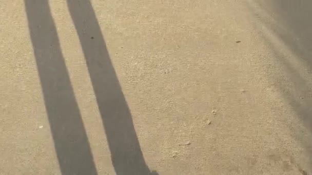 De man loopt langs de weg. Schaduw van de benen tegen de zonsondergang. De camera kijkt naar beneden. Abstract Concept van verbetering, succes, inspanning. — Stockvideo