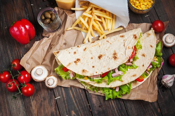 Bükülmüş sandviç Tortilla iki parça ve patates kızartması bir ahşap arka plan üzerinde rulo