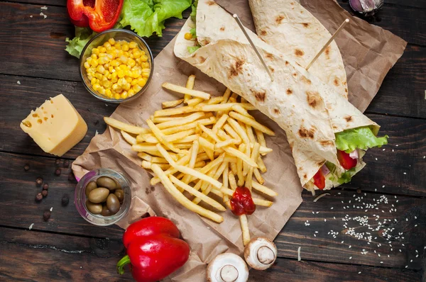 Bükülmüş sandviç Tortilla iki parça ve patates kızartması bir ahşap arka plan üzerinde rulo