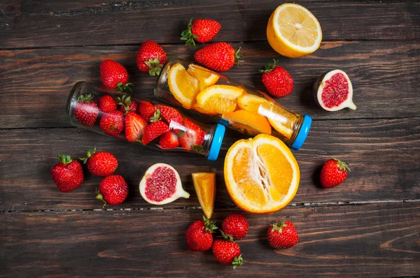 Flaska med skivade apelsiner och jordgubbar på träbord, ekologisk vegan drink — Stockfoto