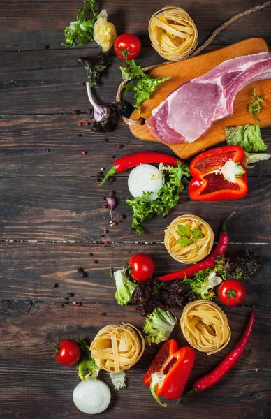 Fondo de la comida italiana, con carne, tomates, espaguetis, ajo, granos de pimienta, chile en la mesa de madera — Foto de Stock