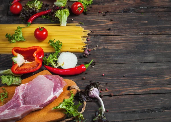 Fondo de la comida italiana, con carne, tomates, espaguetis, ajo, granos de pimienta, chile en la mesa de madera — Foto de Stock