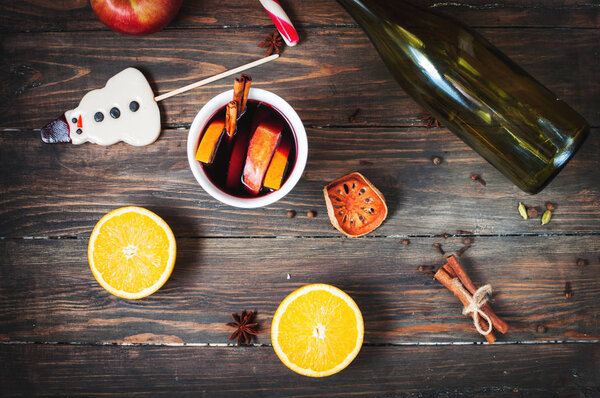 Hot mulled wine with spices, apple and orange on wood background