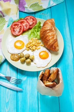 Ahşap bir masaya Servis Kahvaltı. Kızarmış yumurta, domates, kruvasan