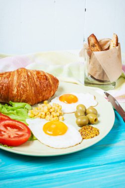 Ahşap bir masaya Servis Kahvaltı. Kızarmış yumurta, domates, kruvasan