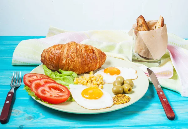 Сніданок на дерев'яному столі. Смажені яйця, помідори, круасан — стокове фото