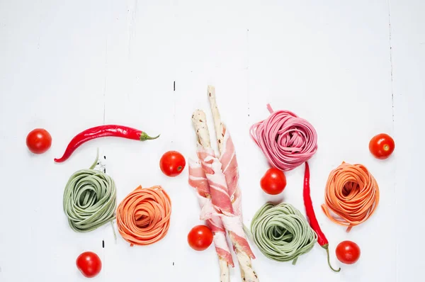 Pasta colorata laminata, pomodorini ciliegini e pancetta sullo sfondo di legno bianco — Foto Stock