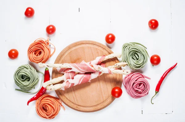 Pasta colorata laminata, pomodorini ciliegini e pancetta sullo sfondo di legno bianco — Foto Stock