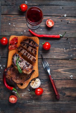 Taze kiraz domates ve kırmızı sıcak biber ile ahşap bir gemide baharatlarla terbiyeli ızgara sığır eti biftek servis
