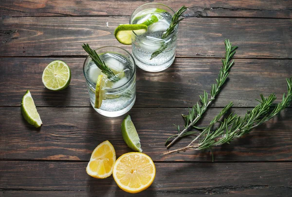 Bevanda alcolica gin tonic cocktail con limone, rosmarino e ghiaccio sul tavolo rustico in legno . — Foto Stock