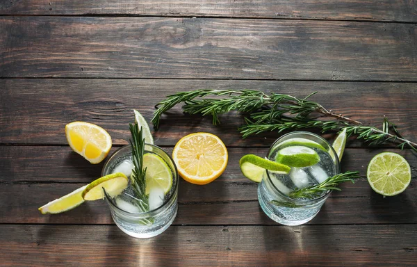 Bevanda alcolica gin tonic cocktail con limone, rosmarino e ghiaccio sul tavolo in legno rustico, spazio per la copia . — Foto Stock