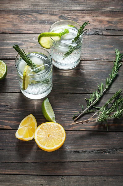 Bevanda alcolica gin tonic cocktail con limone, rosmarino e ghiaccio sul tavolo rustico in legno . — Foto Stock