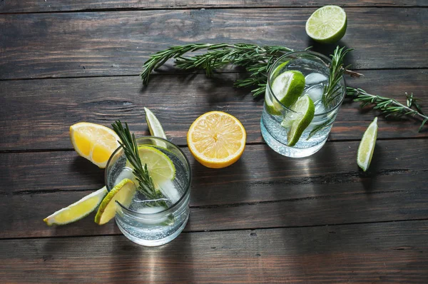 レモン、ローズマリー、素朴な木製のテーブルにアイスとアルコール飲料 — ストック写真