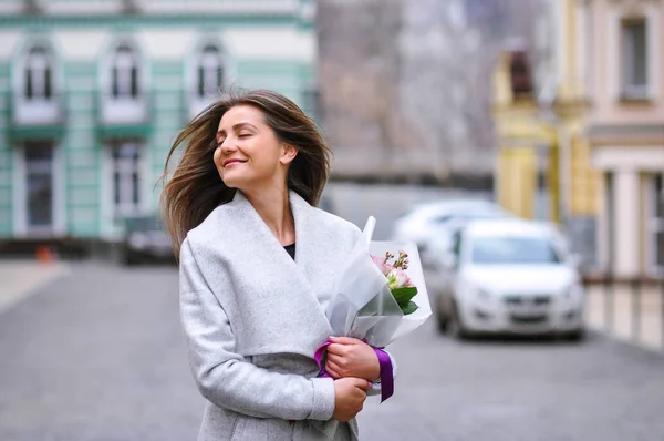Hermosa joven con ramo de flores en la calle de la ciudad. Retrato primaveral de mujer bonita — Foto de Stock