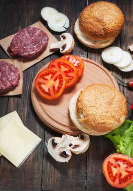 Ev yapımı hamburger malzemeler. Çiğ kıyma, taze ekmek, peynir, domates, soğan, marul ahşap arka plan üzerine dilim