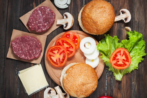 Homemade hamburger ingredients. Raw minced beef, fresh bun, slice of cheese, tomato, onion rings, lettuce on wood background