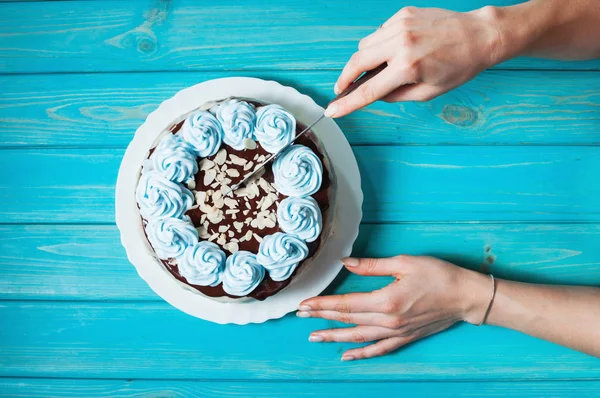 Las manos de la mujer cortan el pastel con crema azul sobre fondo de madera azul . — Foto de Stock