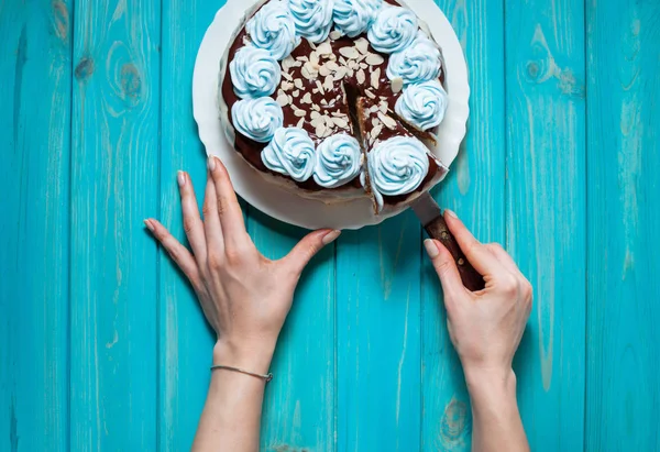 Las manos de la mujer cortan el pastel con crema azul sobre fondo de madera azul . — Foto de Stock