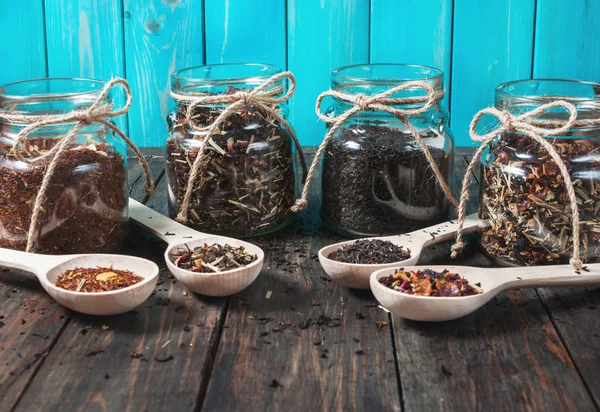 Diferentes tipos de chá em jarra e colheres de madeira na mesa de madeira — Fotografia de Stock