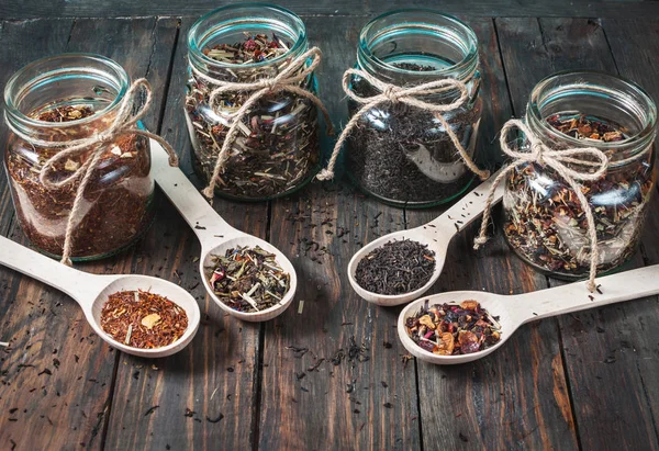 Diferentes tipos de chá em jarra e colheres de madeira na mesa de madeira — Fotografia de Stock