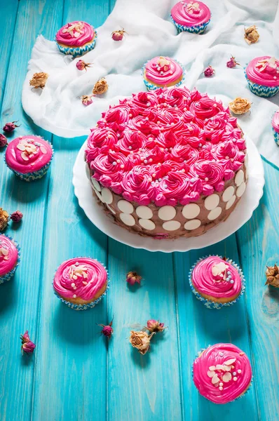 Cake and cupcakes with pink cream on blue wood background. — Stock Photo, Image