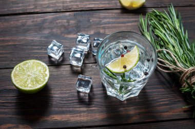 Alcoholic drink - gin tonic cocktail - with lime, rosemary and ice on rustic wooden table clipart