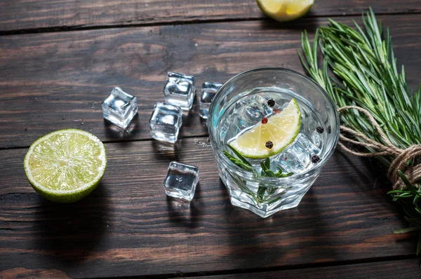 Alcoholic drink - gin tonic cocktail - with lime, rosemary and ice on rustic wooden table — Stock Photo, Image