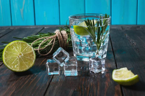ライム、ローズマリー、素朴な木製のテーブルにアイスとアルコール飲料 - ジン トニック カクテル- — ストック写真