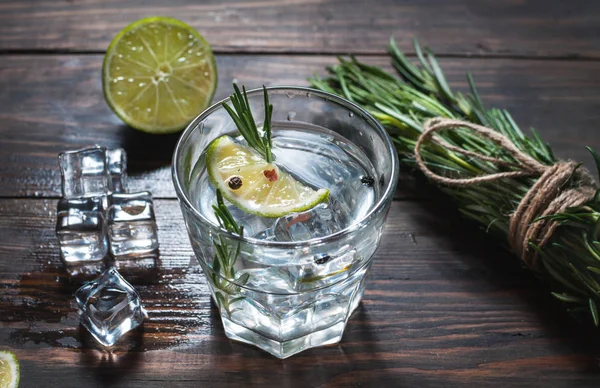 Bevanda alcolica - cocktail tonico al gin - con lime, rosmarino e ghiaccio sul tavolo rustico in legno — Foto Stock