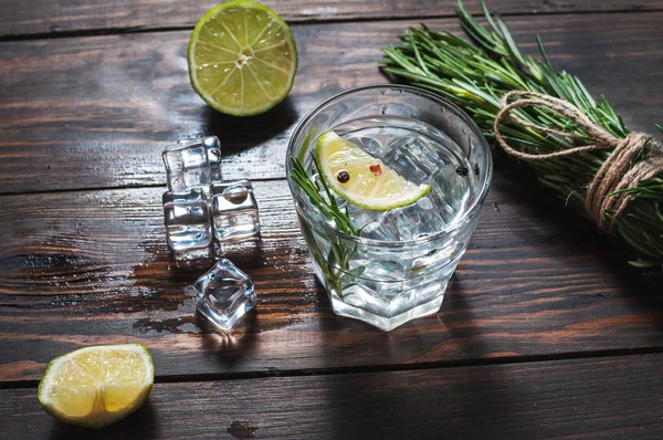 Bevanda alcolica - cocktail tonico al gin - con lime, rosmarino e ghiaccio sul tavolo rustico in legno — Foto Stock