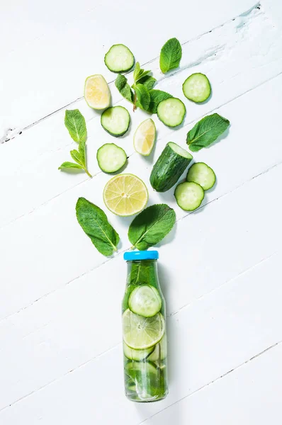 Cold and refreshing infused detox water with lime, mint and cucumber in a bottle on white wood background