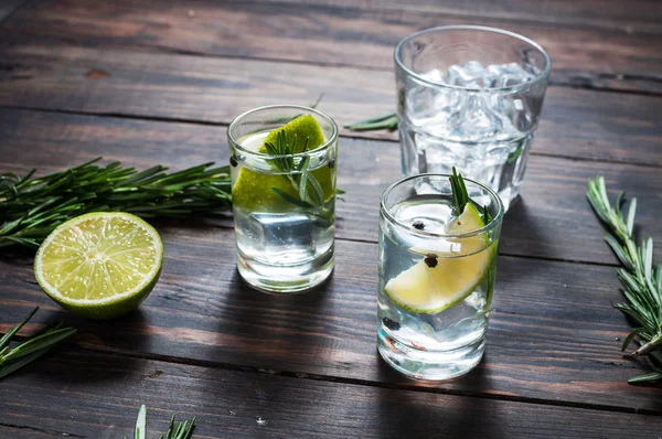 Bevanda alcolica - cocktail tonico al gin - con lime, rosmarino e ghiaccio sul tavolo rustico in legno — Foto Stock