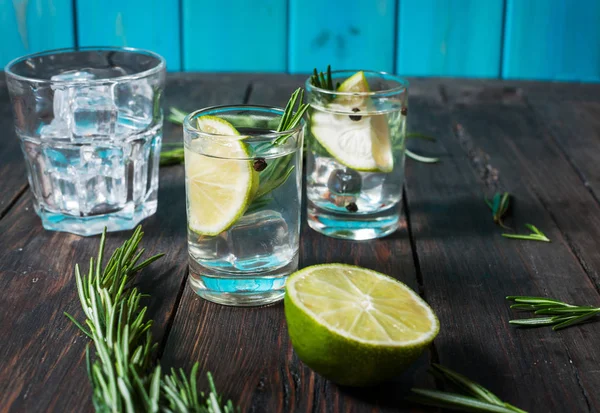 Alcoholic drink - gin tonic cocktail - with lime, rosemary and ice on rustic wooden